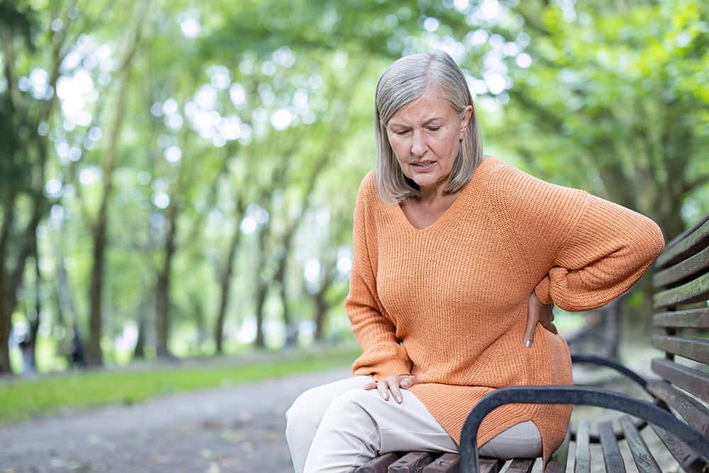 Older woman with back and bladder pain holding her sides while sitting on park bench