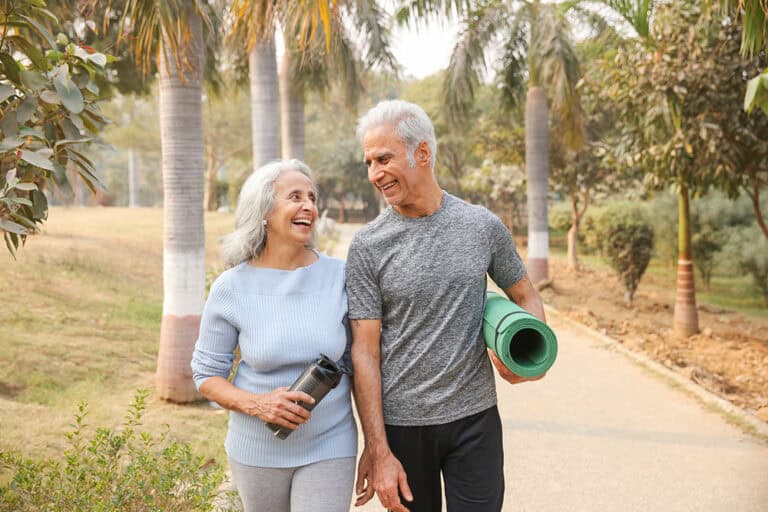 Seniors walking outdoors carrying yoga mat and water cup