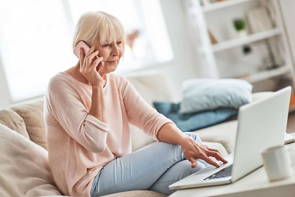 Senior woman sitting on couch with laptop booking appointment for physical therapy