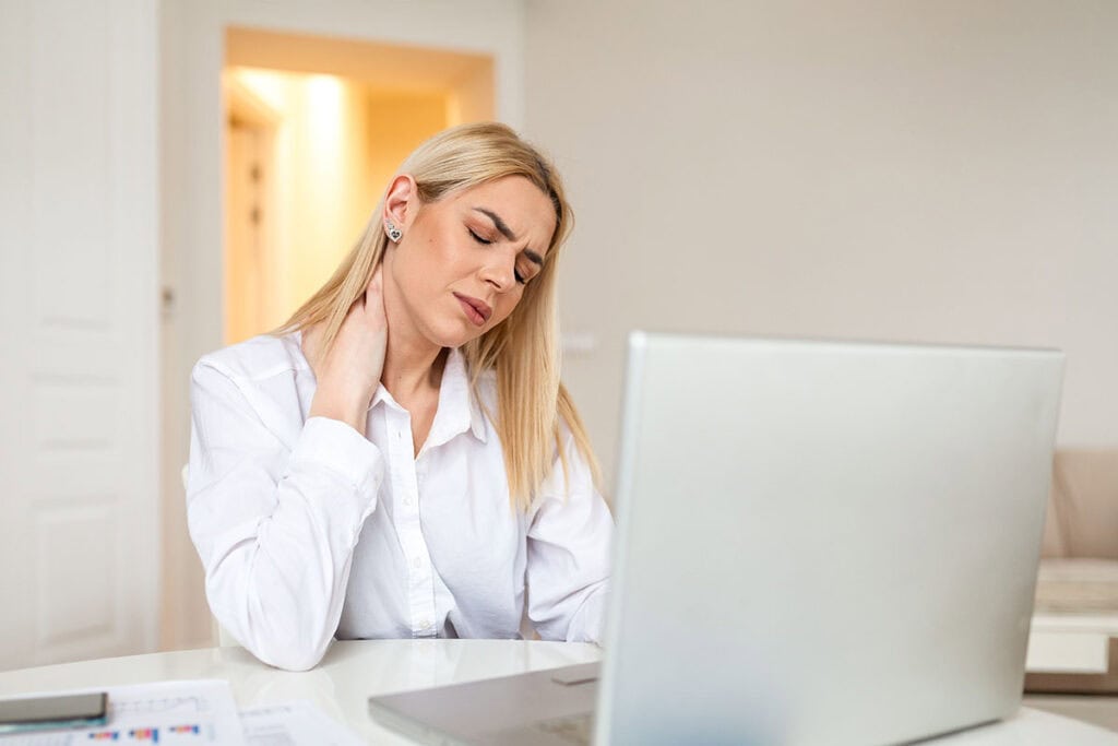Middle aged woman holding her neck in pain from poor posture working from home